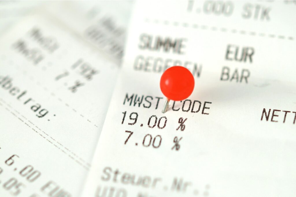 Die Mehrwertsteuer wird auf einem Bon ausgewiesen und mit einer roten Pinnadel hervorgehoben.